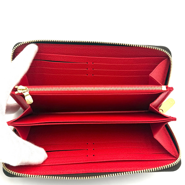 An open black leather zip-around wallet with a bright red interior, shown against a plain white background. A white gloved hand is holding the left side of the wallet open.