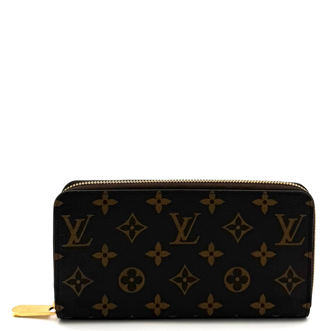 A Louis Vuitton monogram zip-around wallet in black coated canvas with brown monogram motifs and a gold-tone zipper pull, photographed on a white studio background.