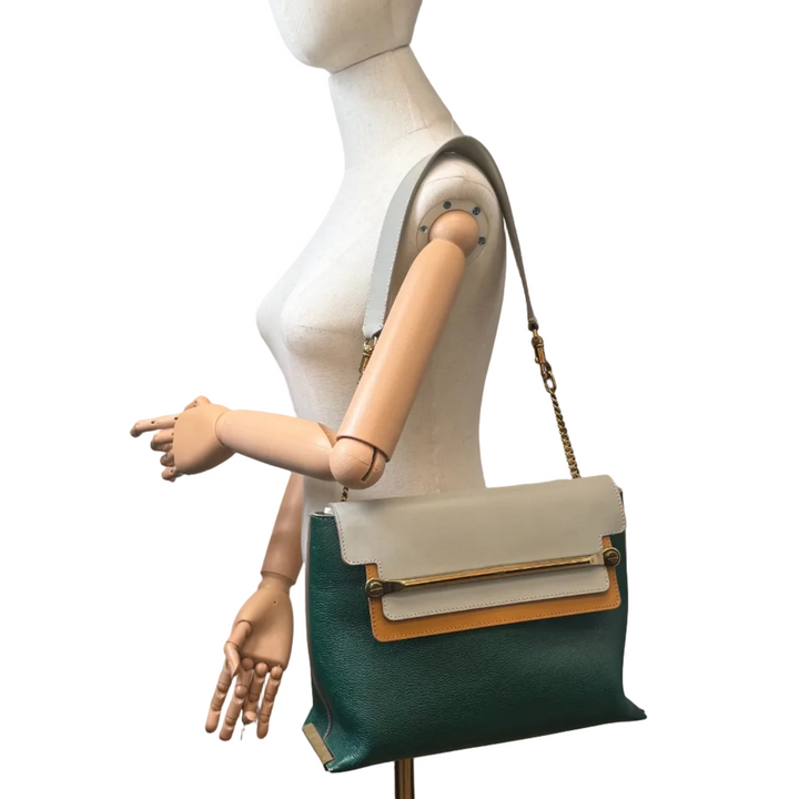 A green and beige leather crossbody bag with gold-tone hardware, shown on a white mannequin torso against a white background.