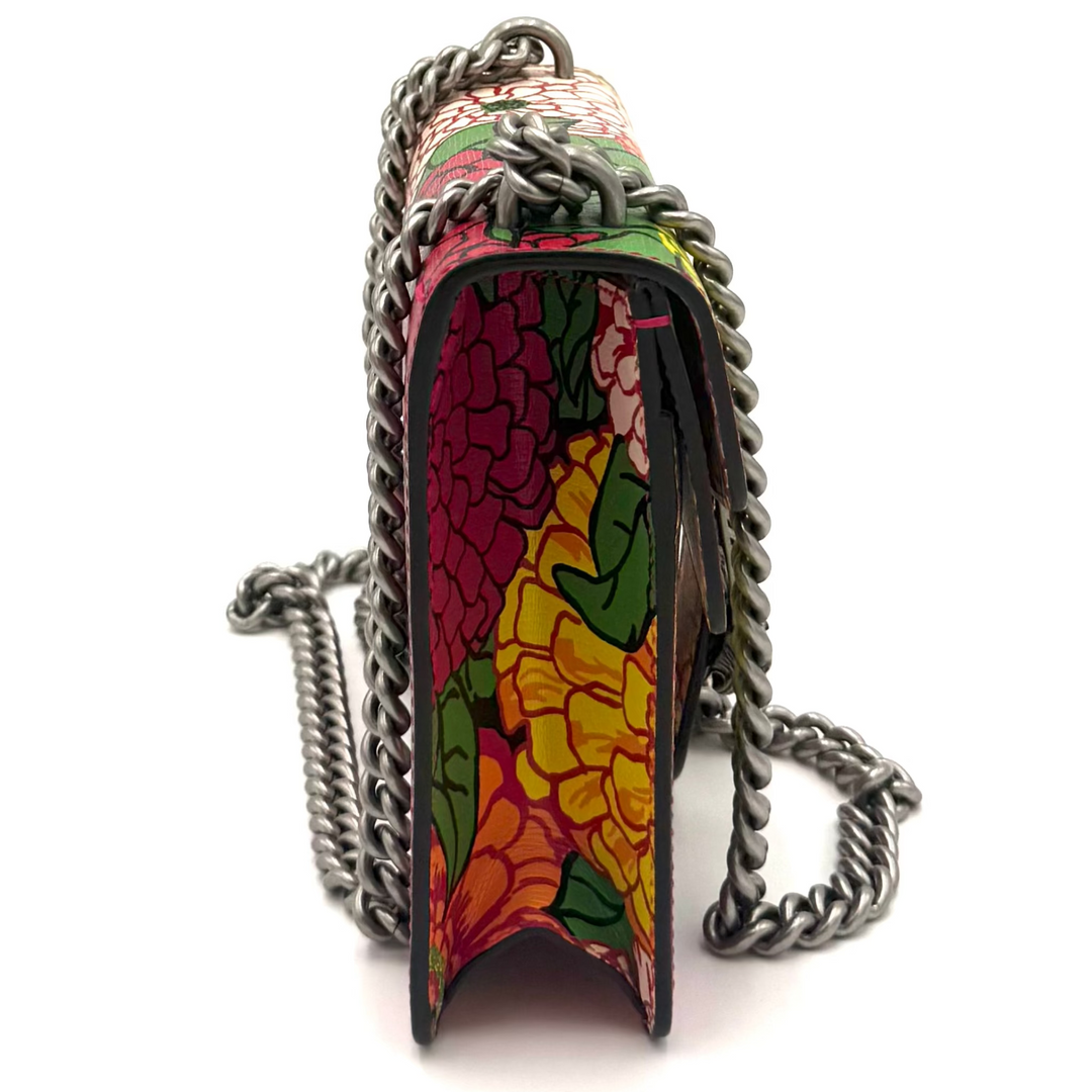 A small handbag with a colorful stained-glass style pattern in red, yellow, green, and pink, featuring a silver chain strap, shown against a plain white background.