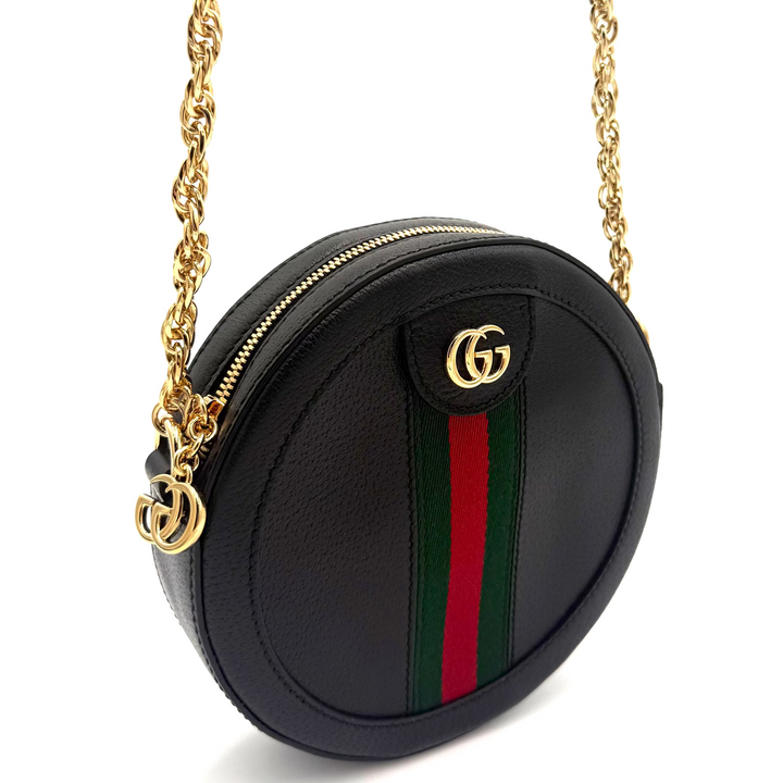 A black leather round crossbody bag with a gold chain strap, featuring the iconic green and red web stripe and a gold interlocking G logo on the front flap.