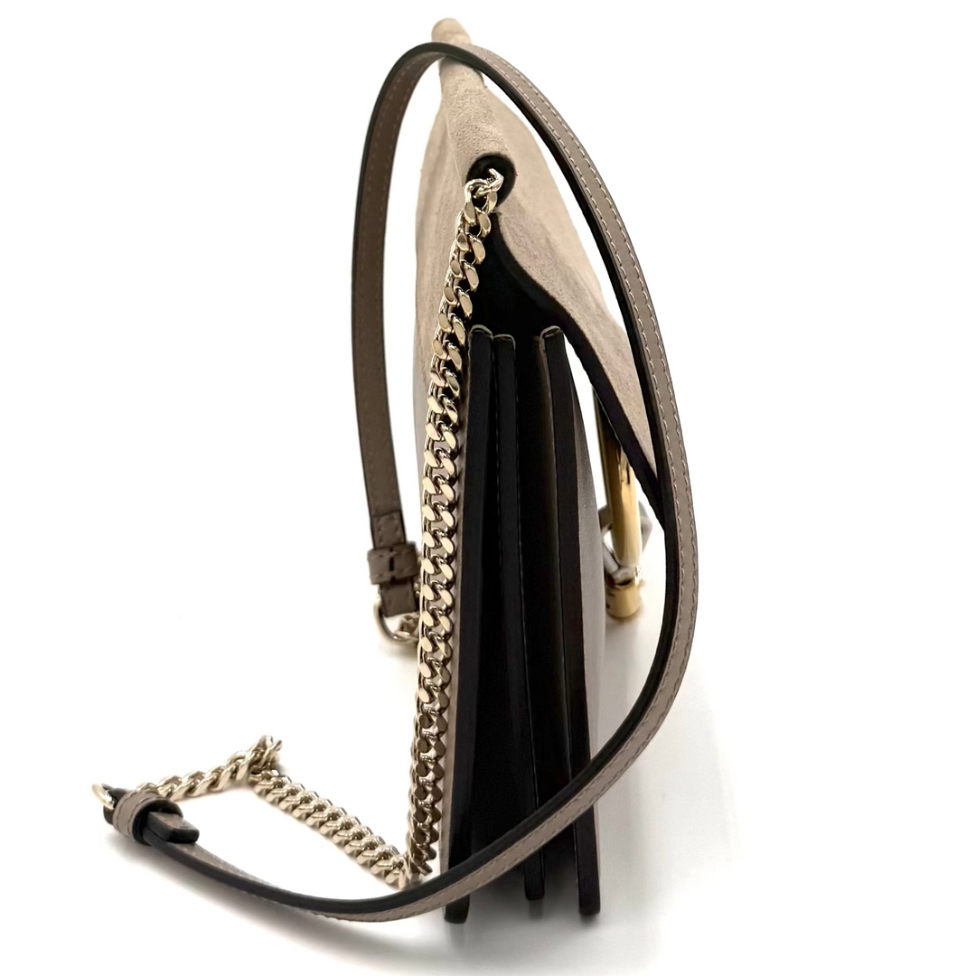 A small black leather shoulder bag with a gold chain strap and tassel detail, shown from a side profile on a white background.