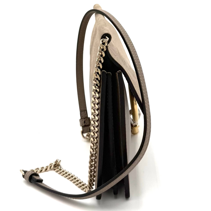 A small black leather shoulder bag with a gold chain strap and tassel detail, shown from a side profile on a white background.