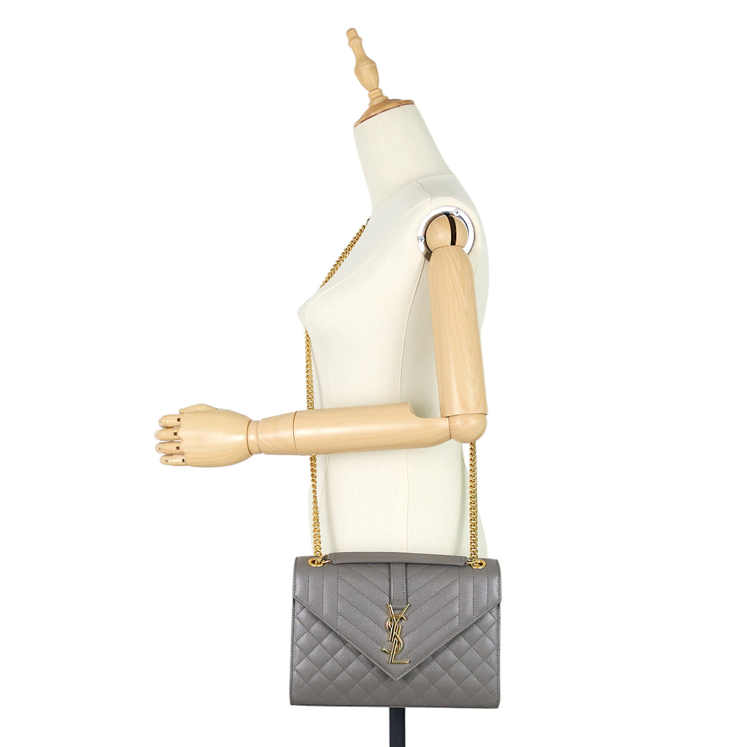 A gray quilted leather shoulder bag with a gold-tone YSL logo and chain strap, displayed on a cream dress form mannequin against a white background.
